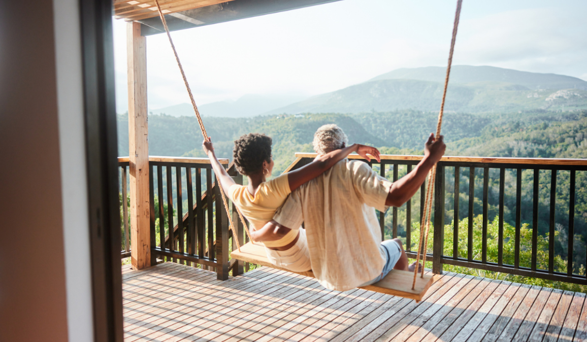 Rear view of a couple sitting together on a swing and looking at the scenic view from the balcony of their vacation rental.
